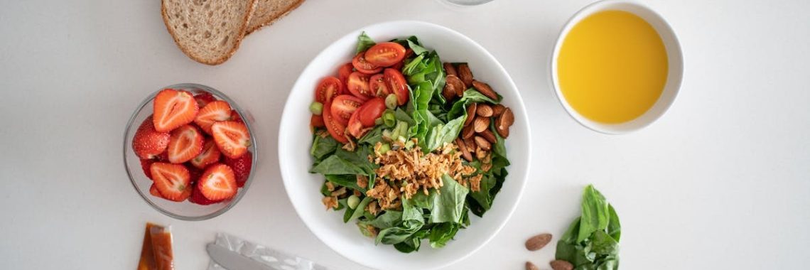 Top view of a healthy salad and fresh ingredients with bread and juice on a white surface.