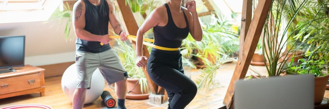 A couple working out on yoga mats indoors, using a laptop for guidance.